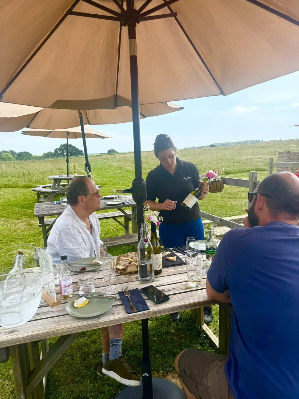 Guests at a table under a parasol as their host pours a tasting