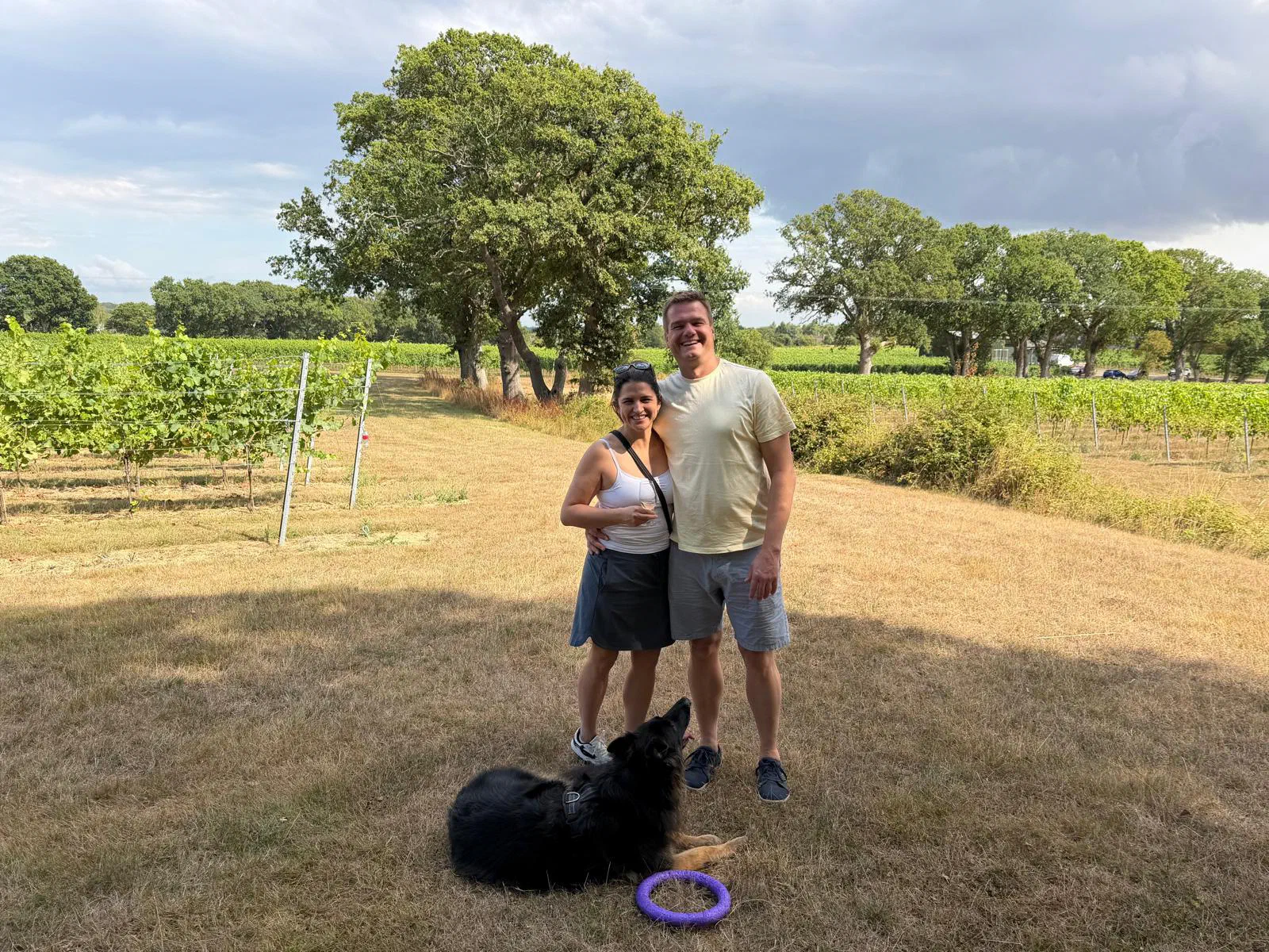 Two guests and a black dog in a vineyard on a sunny day