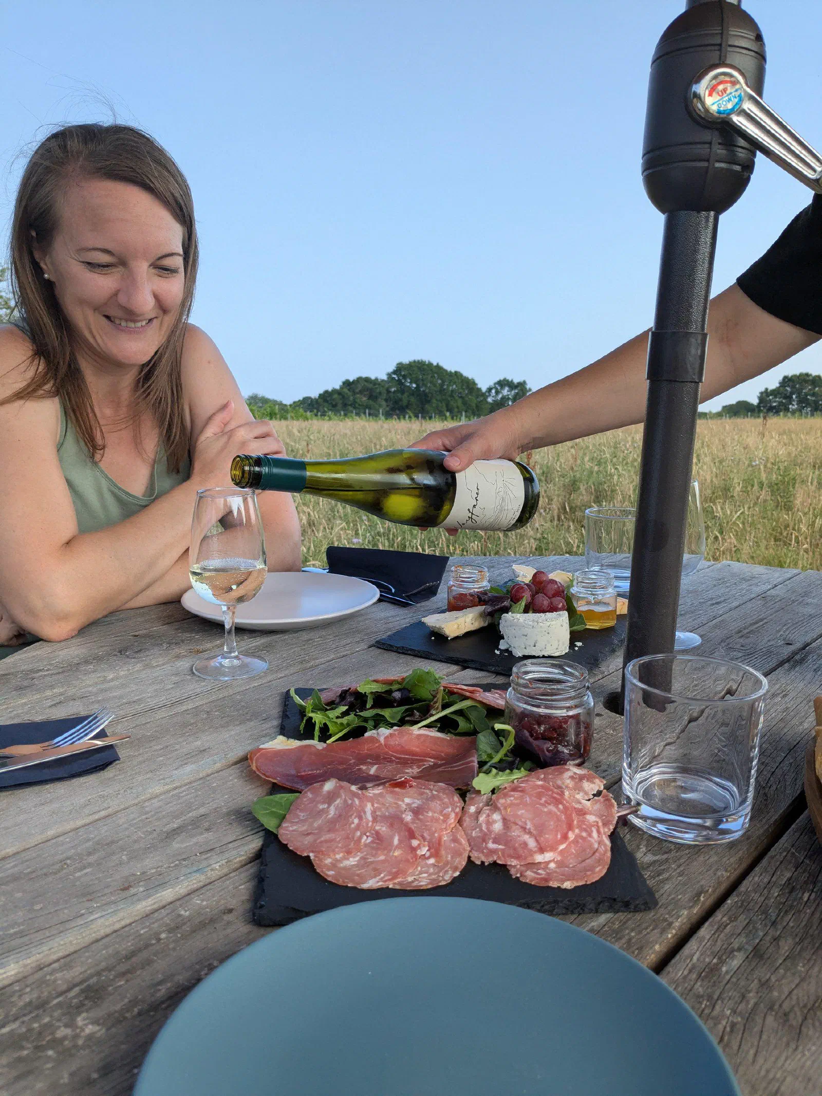 A guest smiling as white wine is poured, with a slate of charcuterie on the table