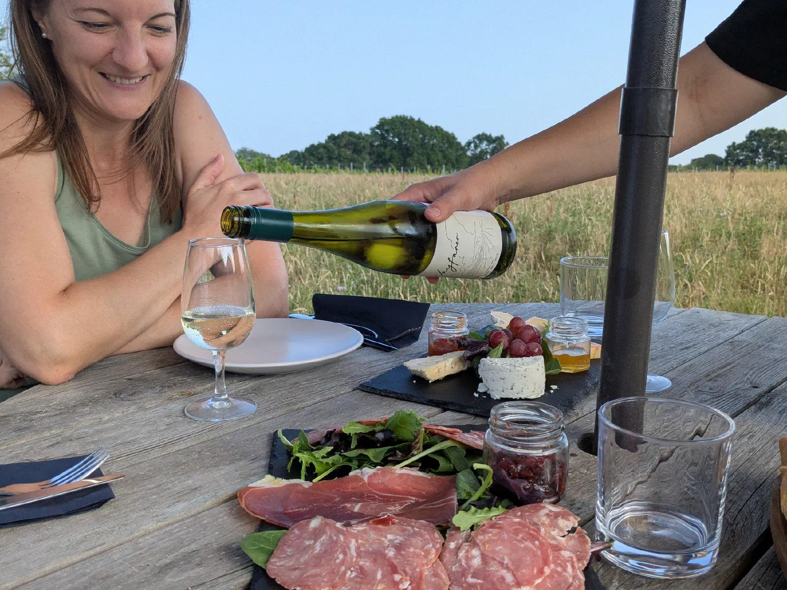 A guest smiling as white wine is poured at Wayfarer, with a slate of charcuterie on the table