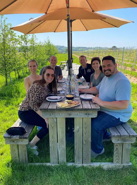 Six guests smiling round a picnic table under two parasols