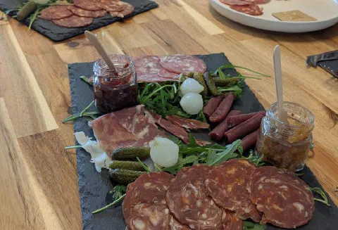 A charcuterie slate with salami, ham, cornichons and two jars of chutney
